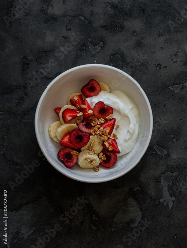 Delicious breakfast, dessert - soft cottage cheese with banana, cherry, strawberry and granola on a dark background, top view