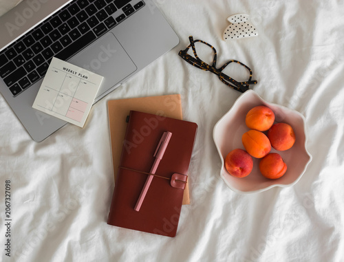 Laptop, notebook, bowl of apricots, glasses on the bed, top view