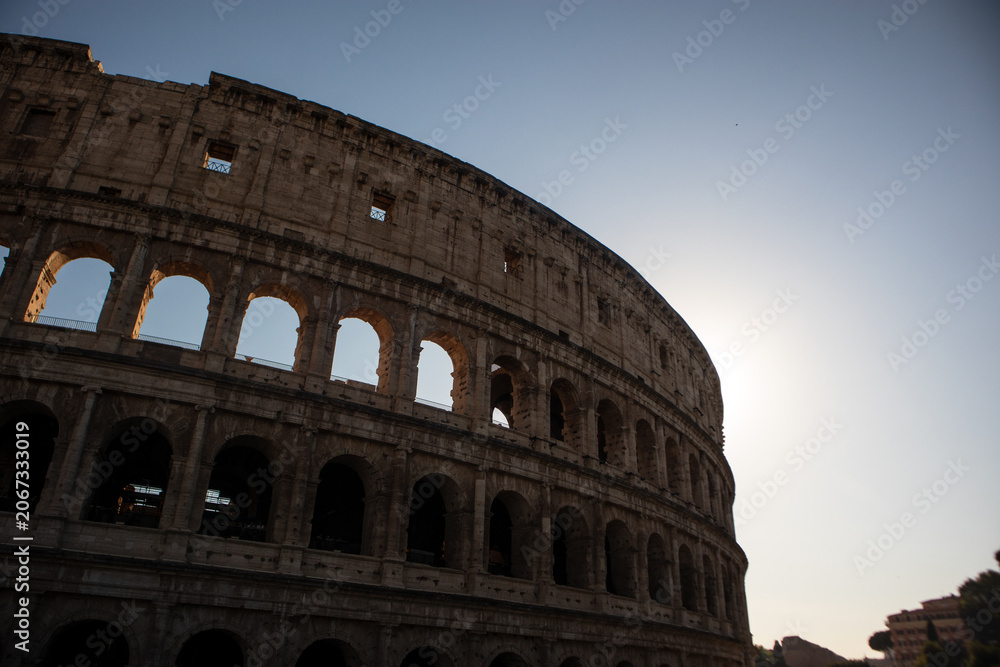 Fototapeta premium Inquadratura dal basso delle storiche arcate del Colosseo a Roma illuminate dalla luce calda del sole, antico monumento romano simbolo dell'Italia e patrimonio dell'umanità UNESCO