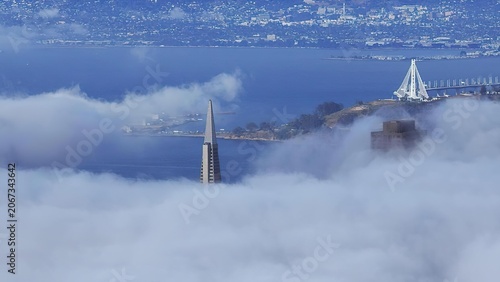 Cuadro en lienzo Tall city skyscraper rising above clouds with a bridge