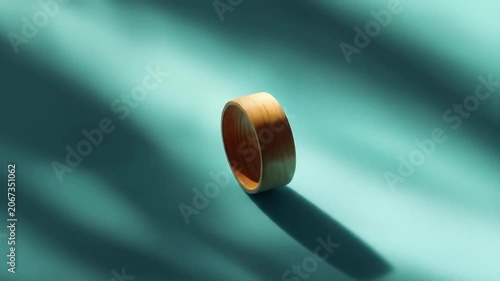 Wooden ring illuminated by sunlight on a teal surface with shadows