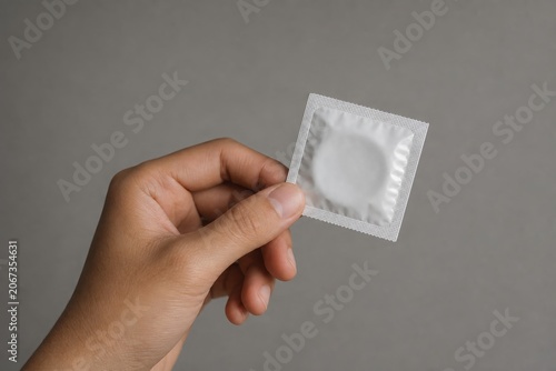 A hand holding a sealed condom packet against a plain gray background.