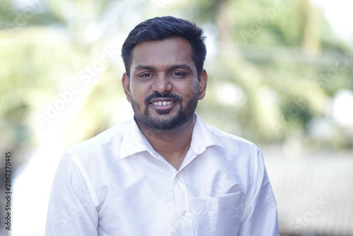 man likely from South India is smiling wearing a white collared shirt.