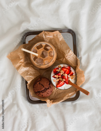 Breakfast in bed - cottage cheese with strawberries, chocolate muffin, ice latte on a metal tray on a light background