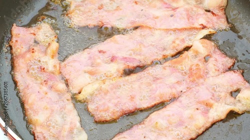 Crispy bacon strips sizzling and bubbling in hot frying pan oil during cooking