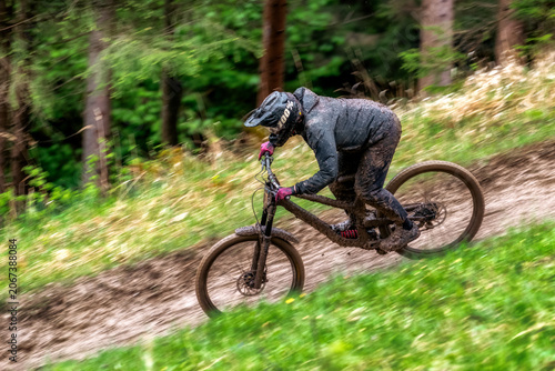 Mud covered downhill mountain biker racing through forest trail with motion blur