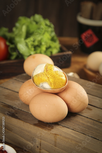 Golden Egg Cracked Open Revealing Rich Yolk on Rustic Wooden Kitchen Table with Fresh Vegetables