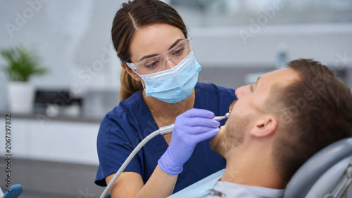 Dental hygienist cleaning patient teeth with scaling instrument in bright modern dental clinic – oral hygiene, professional dental care, preventive dentistry, commercial stock