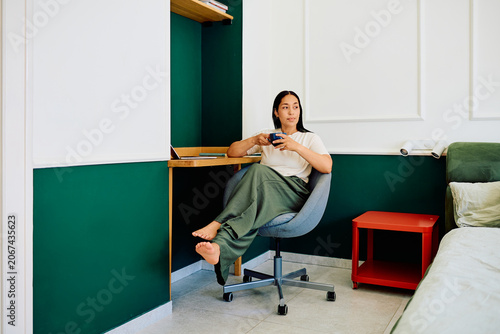 фотографія Young woman sitting comfortably at a minimalist desk, contemplating while enjoyi