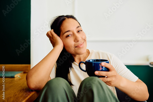 фотографія Woman smiling, relaxing at home, holding a cup of coffee
