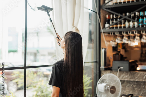 Fotografía Anonymous young trainee wipes restaurant windows with squeegee before opening hours