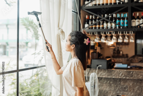 Bild auf Leinwand A young Asian woman on the job trainee wipes restaurant windows with squeegee before opening hours