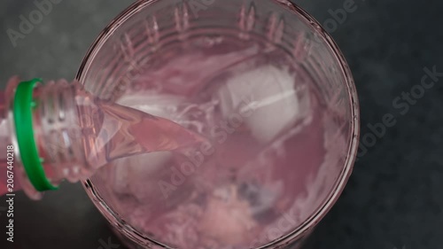 Pouring pink color lemonade in glass with ice, close up