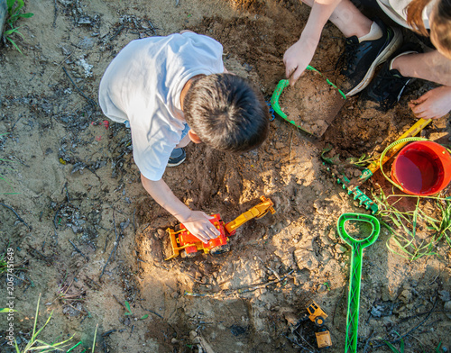 Children playing in the sandbox. Under the evening sun, a child plays in a sandbox with a toy plastic red excavator. Close-up photo without a face, focus on an excavator toy car. High quality photo