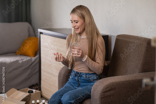 Billede på lærred A young, attractive woman takes vitamins for hair and skin, dietary supplements, and hormone balance for women's health with clean water at home in the living room