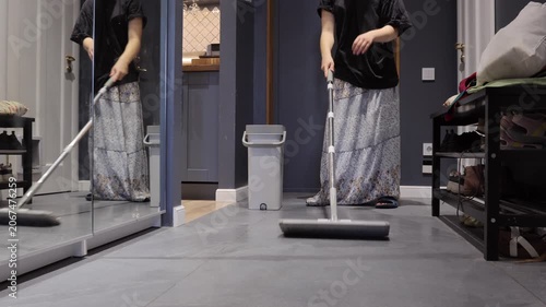 A teenager mops a gray tile hallway beside a gray bucket as part of a daily household chore.