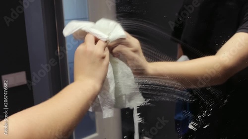 Handheld close-up shows a teenager cleaning a hallway mirror with spray and a paper towel as part of an everyday home cleaning routine.