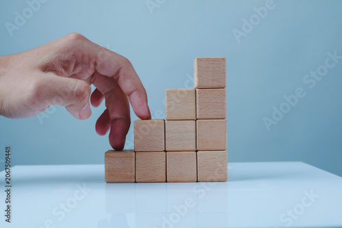 Tableau sur toile Hand arranging wooden blocks into an upward staircase on a blue background, symbolizing business growth, progress, strategy, career development, achievement, and step-by-step success