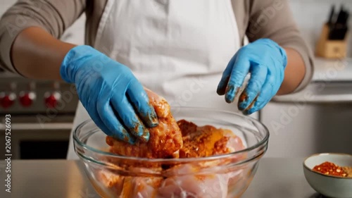 Person seasoning raw chicken with spices, mixing marinade by hand in kitchen