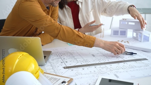 Architects collaborating on building design, analyzing blueprints and a scale model, planning future construction project development with digital tools in an office