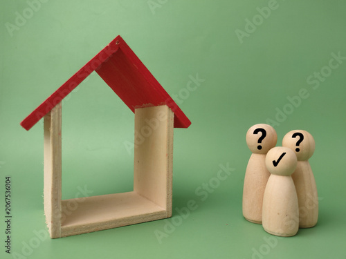 Three wooden figures with question or check marks stand beside an empty wooden house frame with a red roof