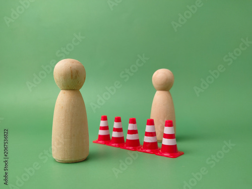 A row of five red and white traffic cones separates two wooden peg figures on a green background