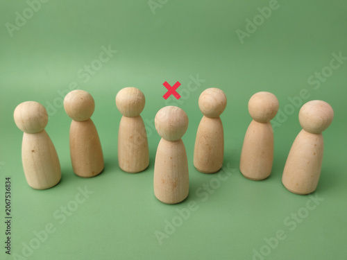 Seven wooden peg figures stand in a row on green, with one figure highlighted by a red cross mark