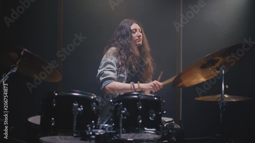 Young drummer girl counts down rhythm with drumsticks, and song starts. Female musician with long curly hair plays a drum kit. Rock band on concert, live on rehearsal room. Repetition in slow motion