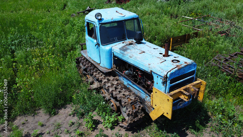 Slika na platnu Old rusty blue tracked tractor standing in a rural field on a sunny summer day