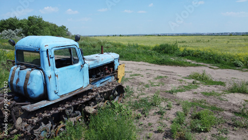Old rusty blue tracked tractor standing in a rural field on a sunny summer day