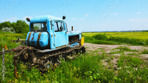Old rusty blue tracked tractor standing in a rural field on a sunny summer day