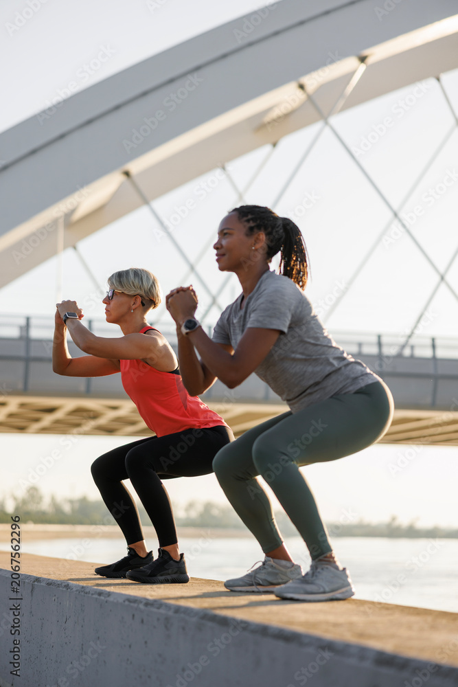 Naklejka premium Fit women doing squats while working out outdoors by the river
