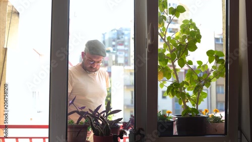 Handsome hipster man watering flowers on a terrace window
