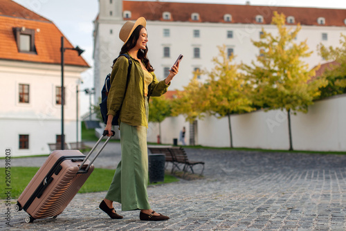 Photos Woman walking with suitcase, looking at her cellphone in city, free space