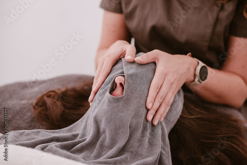Beauty salon, a woman's face is cleaned with a special grey coloured facial towel that is wrapped around the head during a facial inside a room.
