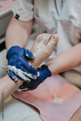 Feet care, vertical image a pedicurist wearing blue gloves for hygiene is performing foot care on a female client inside a feet spa clinic.