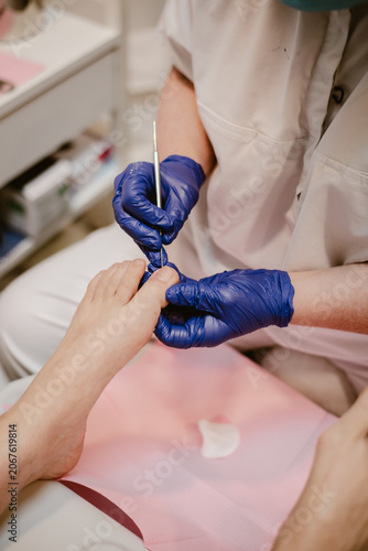 Feet care, vertical image a pedicurist wearing blue gloves for hygiene is performing foot care on a female client inside a feet spa clinic.