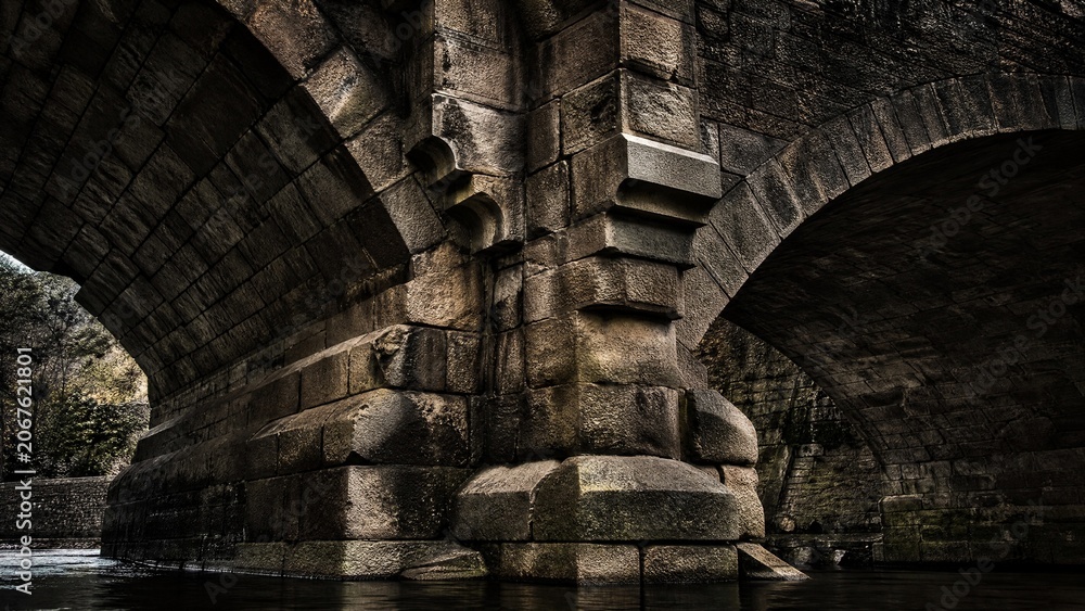 Naklejka premium Underside of an ancient stone arch bridge with massive interlocking blocks and dramatic light.