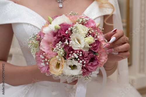 A bride holding a bouquet of pink and white roses in her hands.