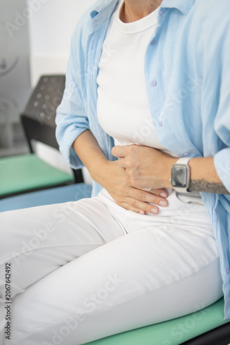 Woman suffering from severe abdominal pain and cramps, touching her stomach with both hands, experiencing discomfort, sickness, and needing relief from a health issue