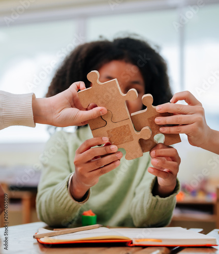 Diverse students hands connecting wooden jigsaw puzzle pieces together on desk during classroom activity within school building