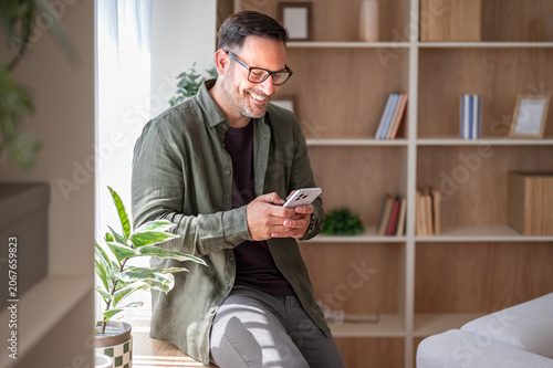 Smiling man relaxing at home, enjoying wireless social media connection, holding a mobile device and actively messaging friends on a communication application