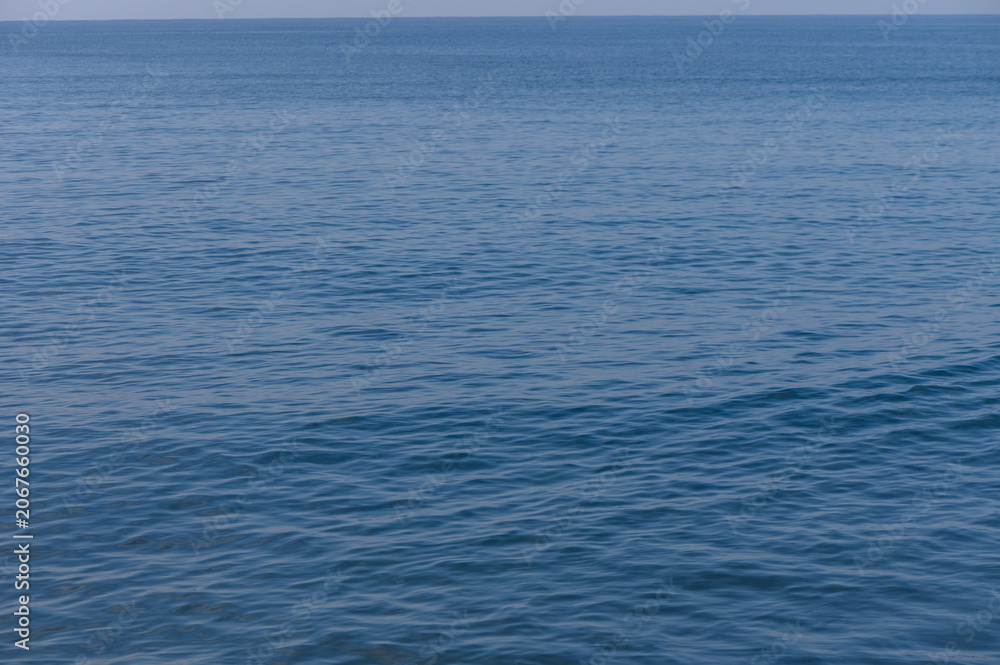 Naklejka premium Calm blue sea stretches endlessly under a clear sky with gentle waves lapping at the shore