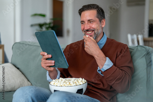 Tableau sur toile Cheerful man binge watching sport on tablet, eating popcorn