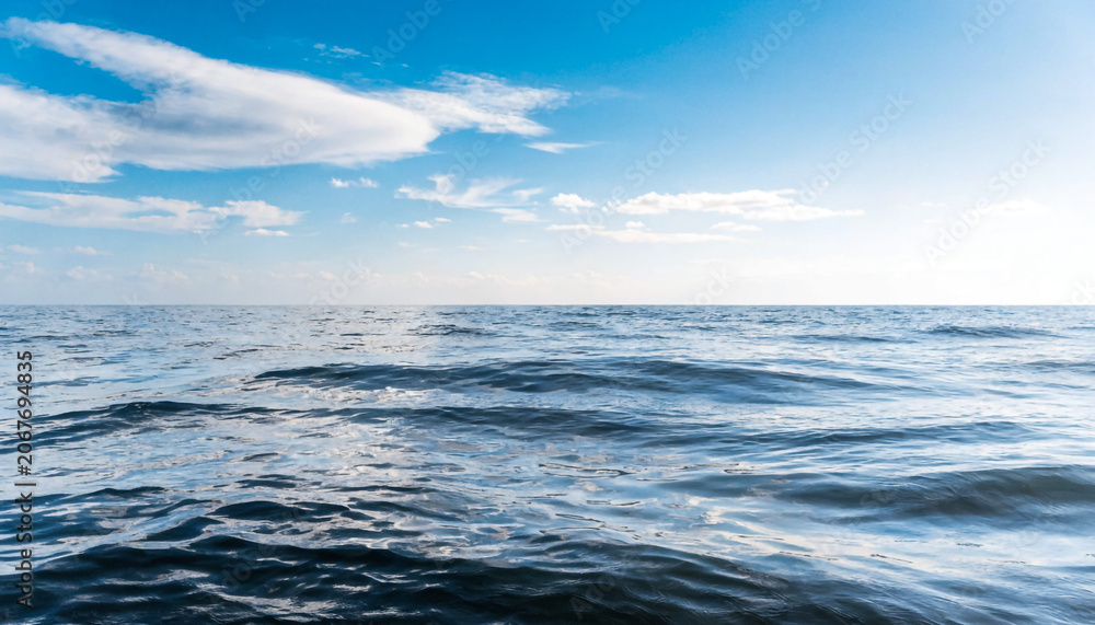 Obraz premium Calm Ocean Waves Under Clear Blue Sky with Soft Clouds Scattered Horizon View