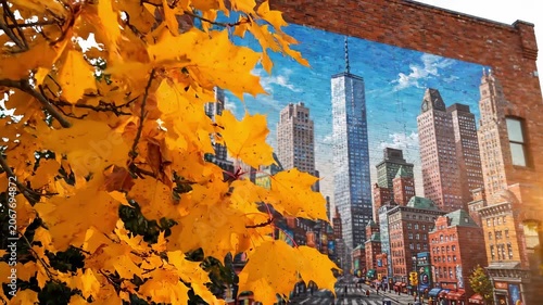 Golden leaves drape over a bustling city mural that showcases majestic skyscrapers. The warm autumn colors bring life to the urban scene, making the city pulse with energy and creativity.