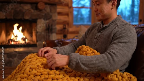 A serene scene unfolds in a snug cabin, where a person sits wrapped in a thick golden blanket, feeling the warmth of a crackling fire. The calm atmosphere invites relaxation and peace.