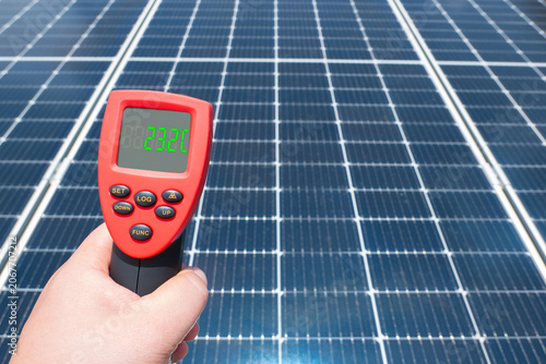 Hand holding infrared thermometer measuring surface temperature of solar panel array outdoors