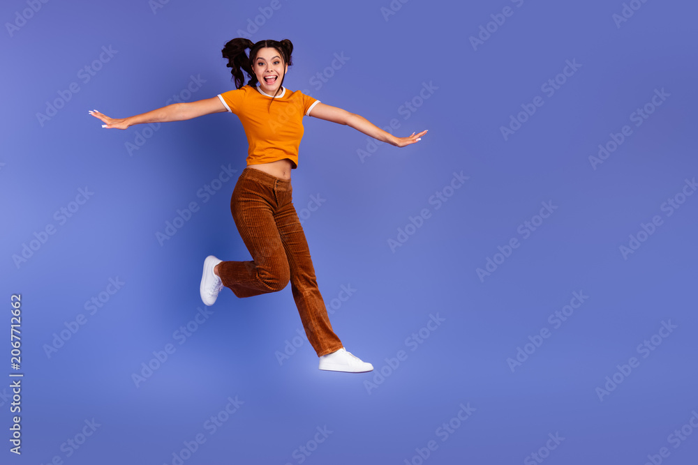 Naklejka premium Joyful young female teen jumps in a stylish casual outfit against a purple background for lifestyle advertising and fashion promotion