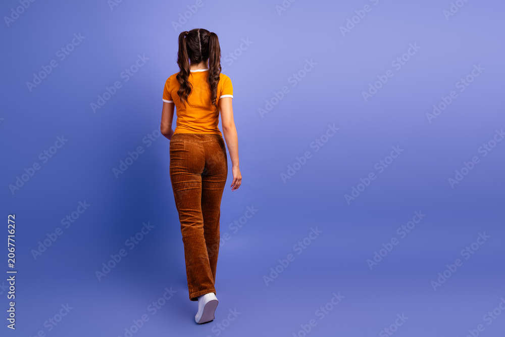 Naklejka premium Young female teen model walks away on a purple studio backdrop showcasing casual fashion lifestyle and a playful mood